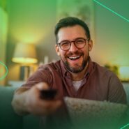 Homem sorridente assistindo TV com pipoca