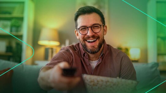 Homem sorridente assistindo TV com pipoca