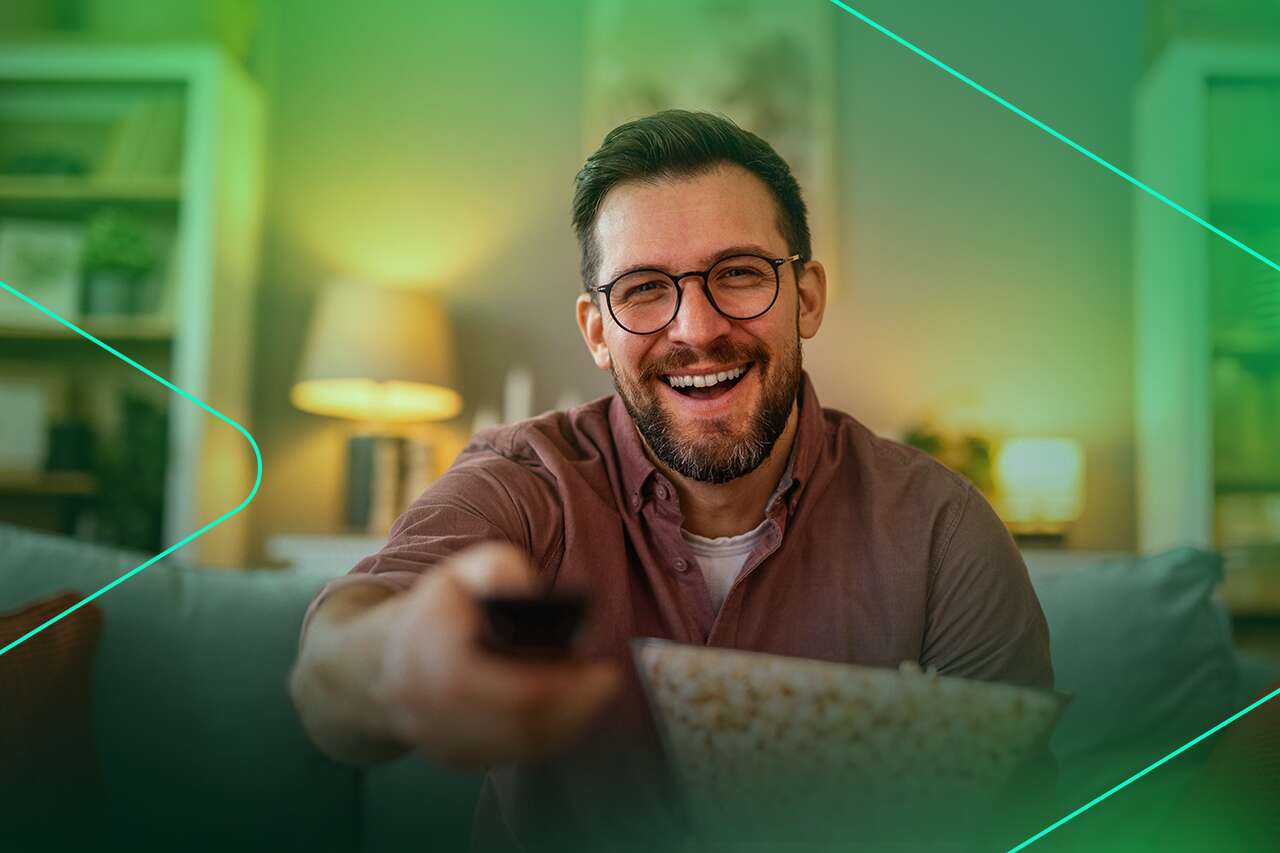 Homem sorridente assistindo TV com pipoca