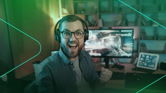 Homem sorrindo e jogando no computador com fones