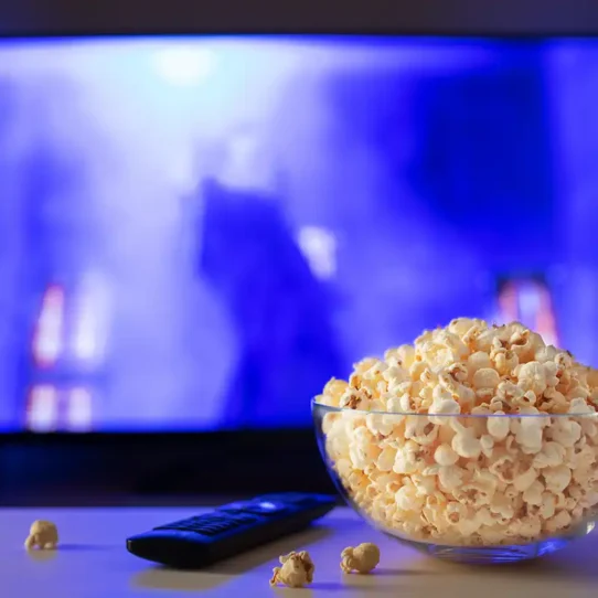 Televisão com um balde de pipoca e controle acima da mesa