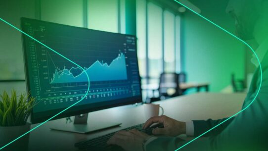 Homem analisando gráficos em monitor de escritório moderno.