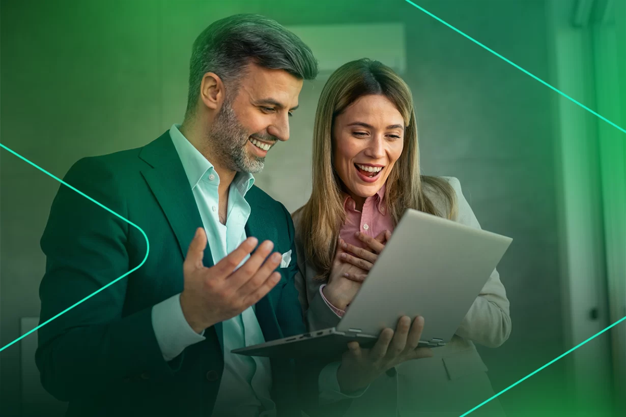 Casal animado olhando para laptop em ambiente de trabalho.
