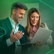 Casal animado olhando para laptop em ambiente de trabalho.