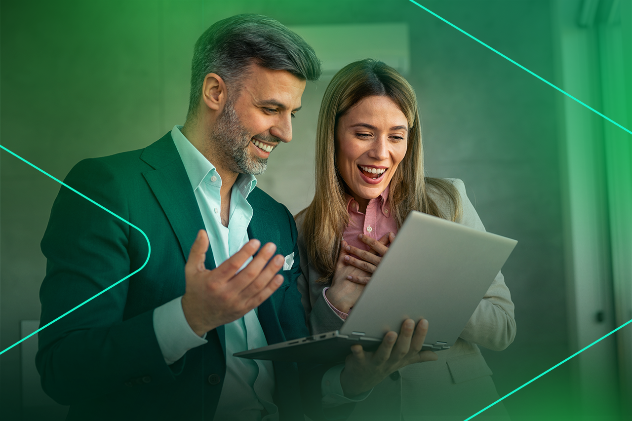 Casal animado olhando para laptop em ambiente de trabalho.