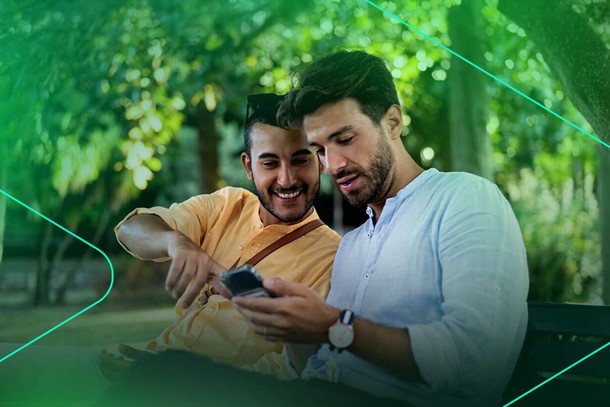 Dois homens sorrindo e usando smartphone em parque