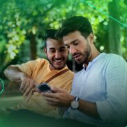 Dois homens sorrindo e usando smartphone em parque