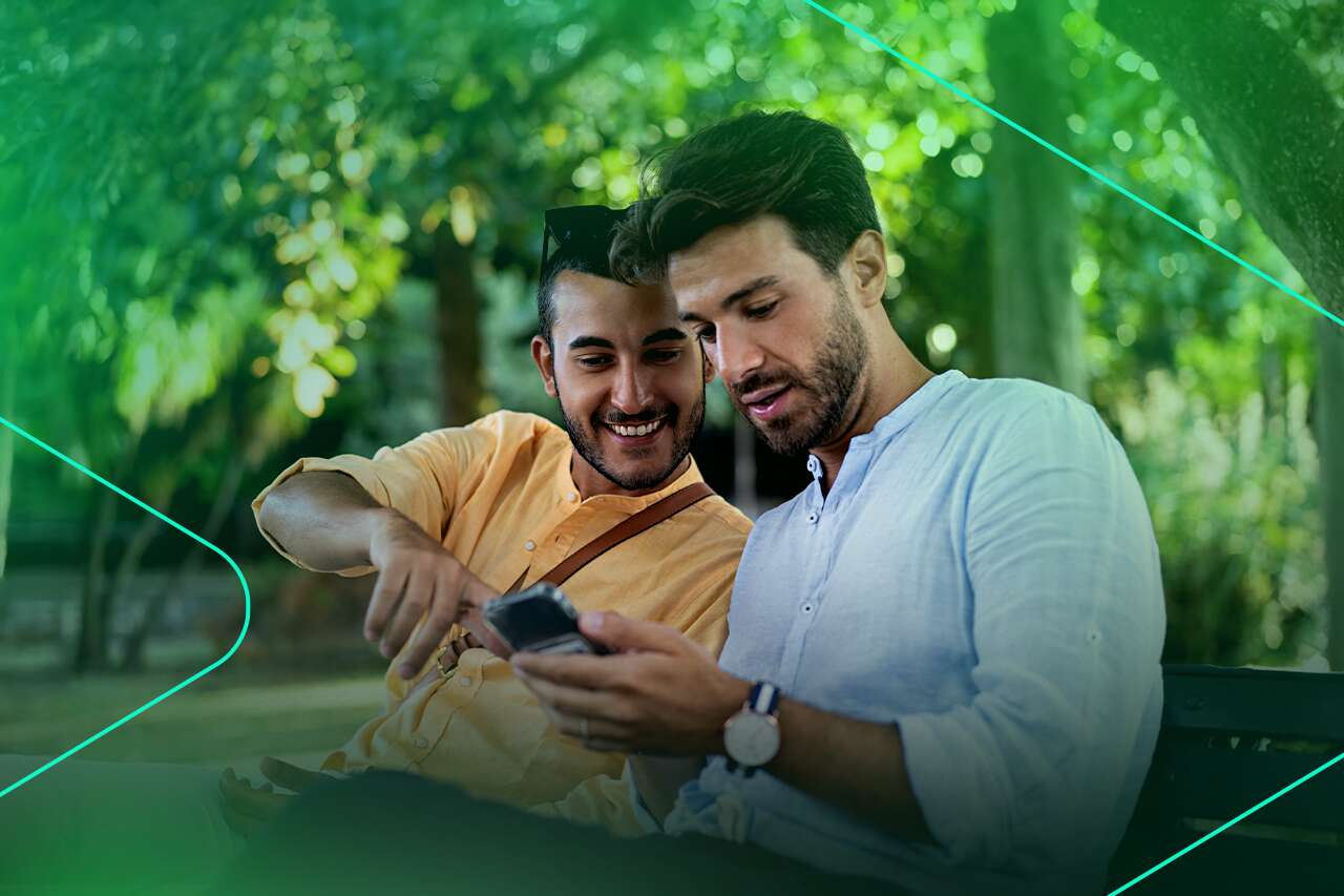 Dois homens sorrindo e usando smartphone em parque