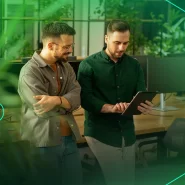 Dois homens analisam dados em tablet em ambiente moderno.