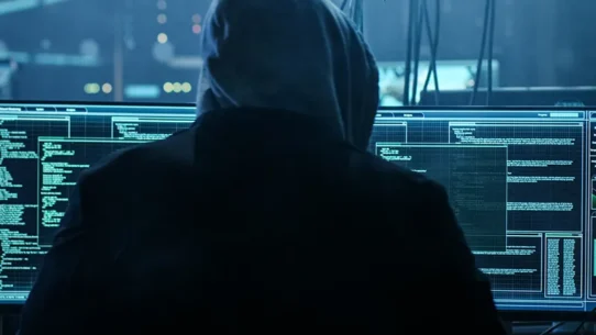 Homem encapuzado interagindo com computadores