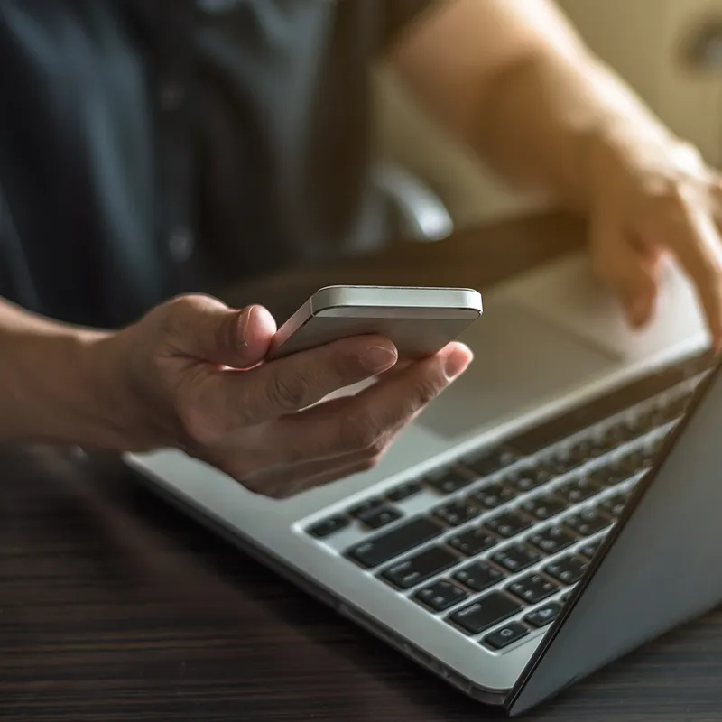 Pessoa interagindo em um notebook com o celular na mão