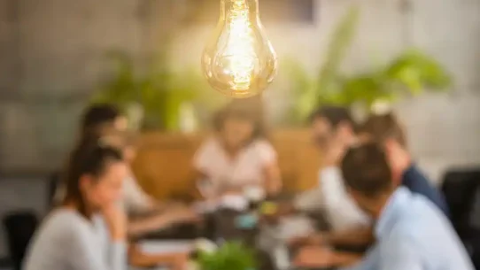 Um grupo de pessoas em reunião, com uma lâmpada iluminando a sala, em foco no centro.