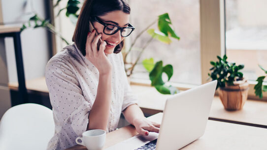Mulher conversando ao telefone e interagindo com o notebook