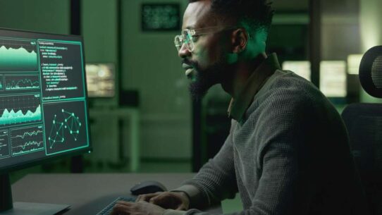 Homem trabalhando em computador com dados em tela.