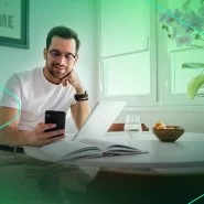 Homem usando celular em mesa com laptop e flores
