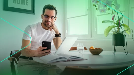 Homem usando celular em mesa com laptop e flores