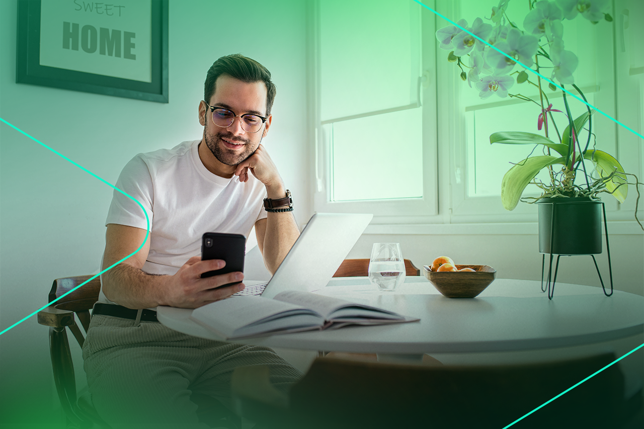 Homem usando celular em mesa com laptop e flores