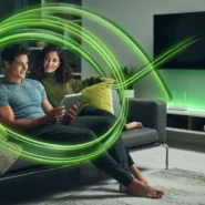 Casal assistindo TV com tablet em sofá moderno.