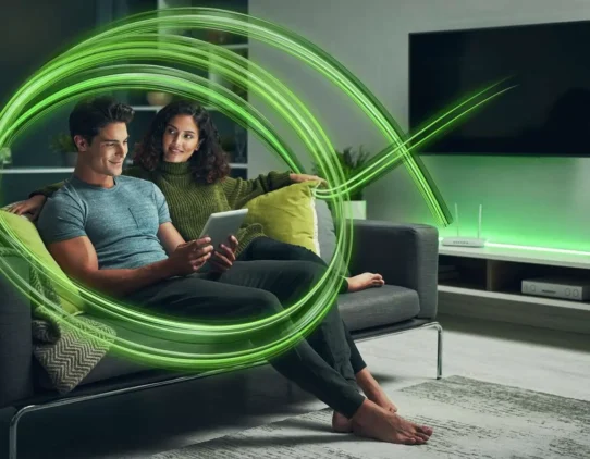 Casal assistindo TV com tablet em sofá moderno.