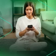 Mulher sentada no chão usando smartphone em casa