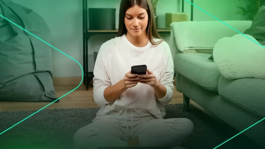 Mulher sentada no chão usando smartphone em casa