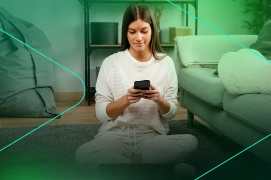 Mulher sentada no chão usando smartphone em casa