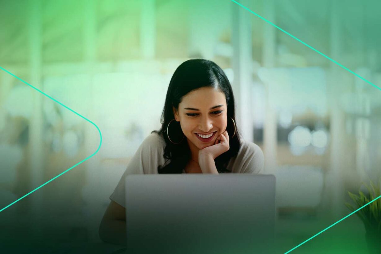 Mulher sorrindo enquanto usa laptop em ambiente de escritório.