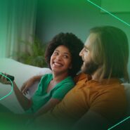 Casal sorrindo enquanto assiste TV no sofá.