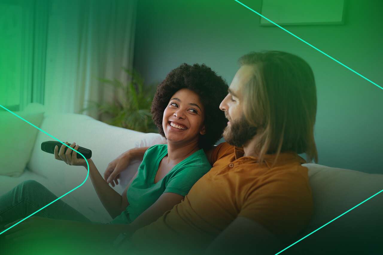 Casal sorrindo enquanto assiste TV no sofá.