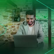 Homem sorrindo trabalhando em laptop na cozinha