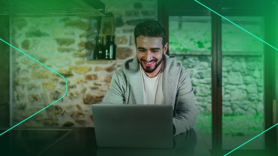 Homem sorrindo trabalhando em laptop na cozinha