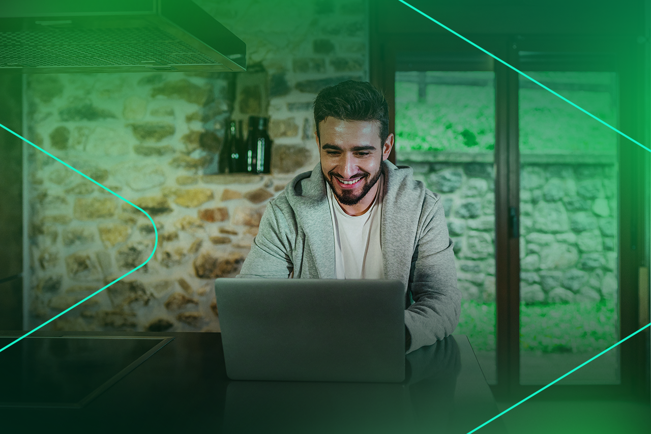 Homem sorrindo trabalhando em laptop na cozinha