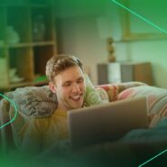 Homem sorrindo enquanto usa laptop no sofá