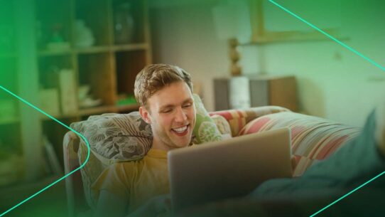 Homem sorrindo enquanto usa laptop no sofá