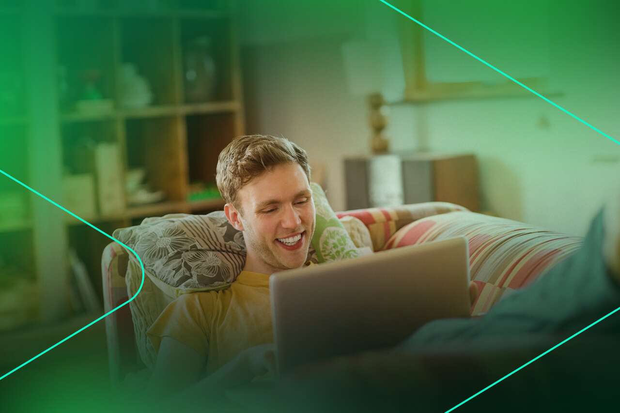 Homem sorrindo enquanto usa laptop no sofá