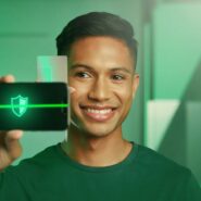Homem sorrindo enquanto segura um smartphone com ícone de segurança.