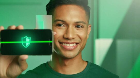 Homem sorrindo enquanto segura um smartphone com ícone de segurança.