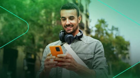 Homem sorrindo enquanto usa celular na rua