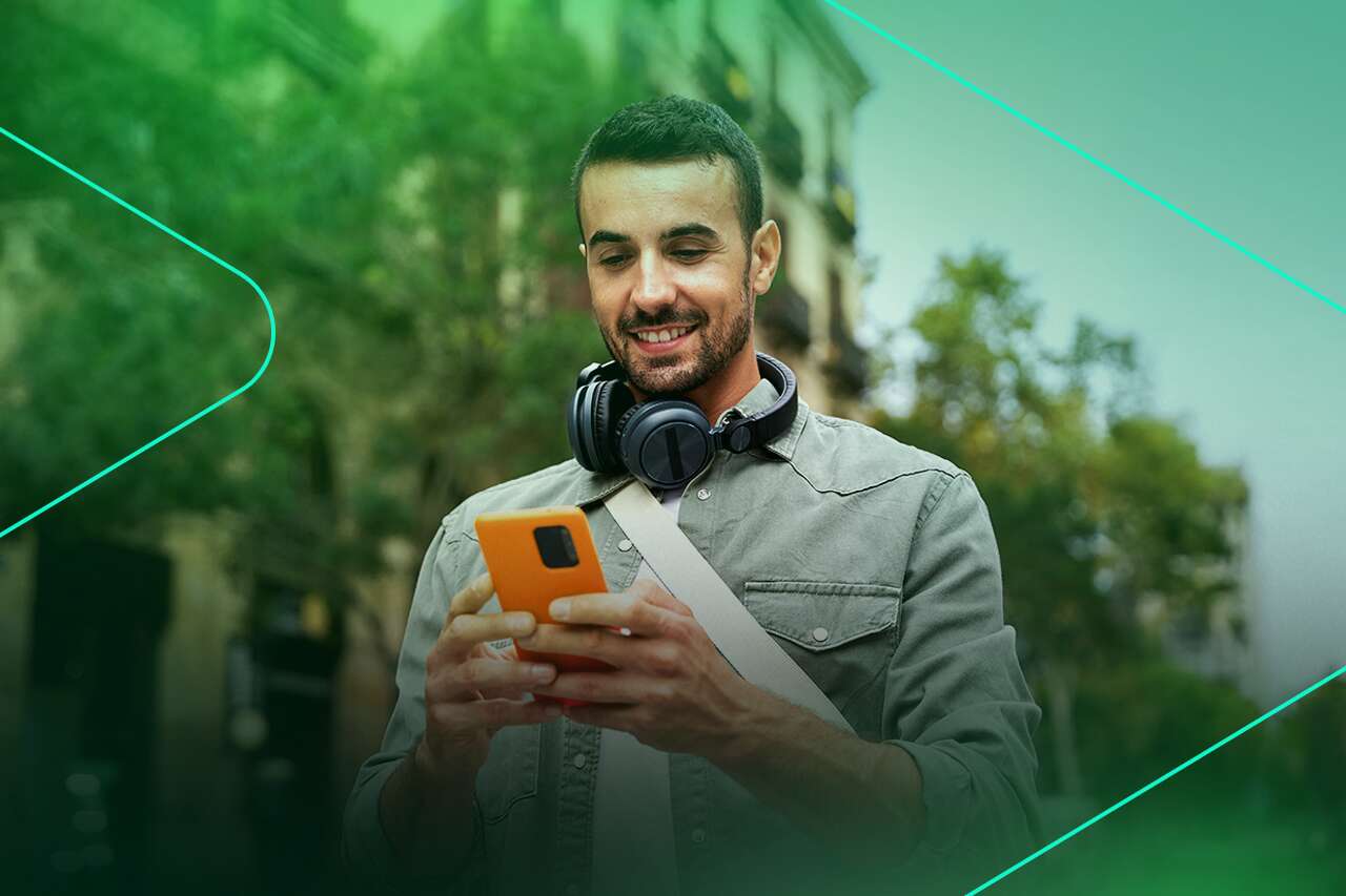 Homem sorrindo enquanto usa celular na rua