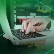 Mão digitando em um laptop com servidores ao fundo