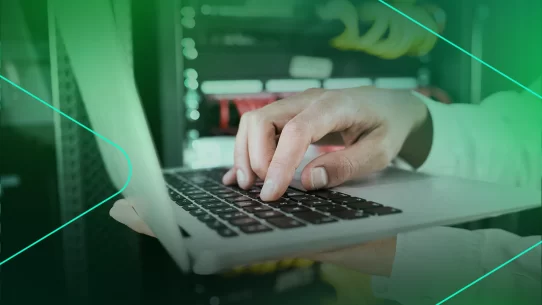 Mão digitando em um laptop com servidores ao fundo