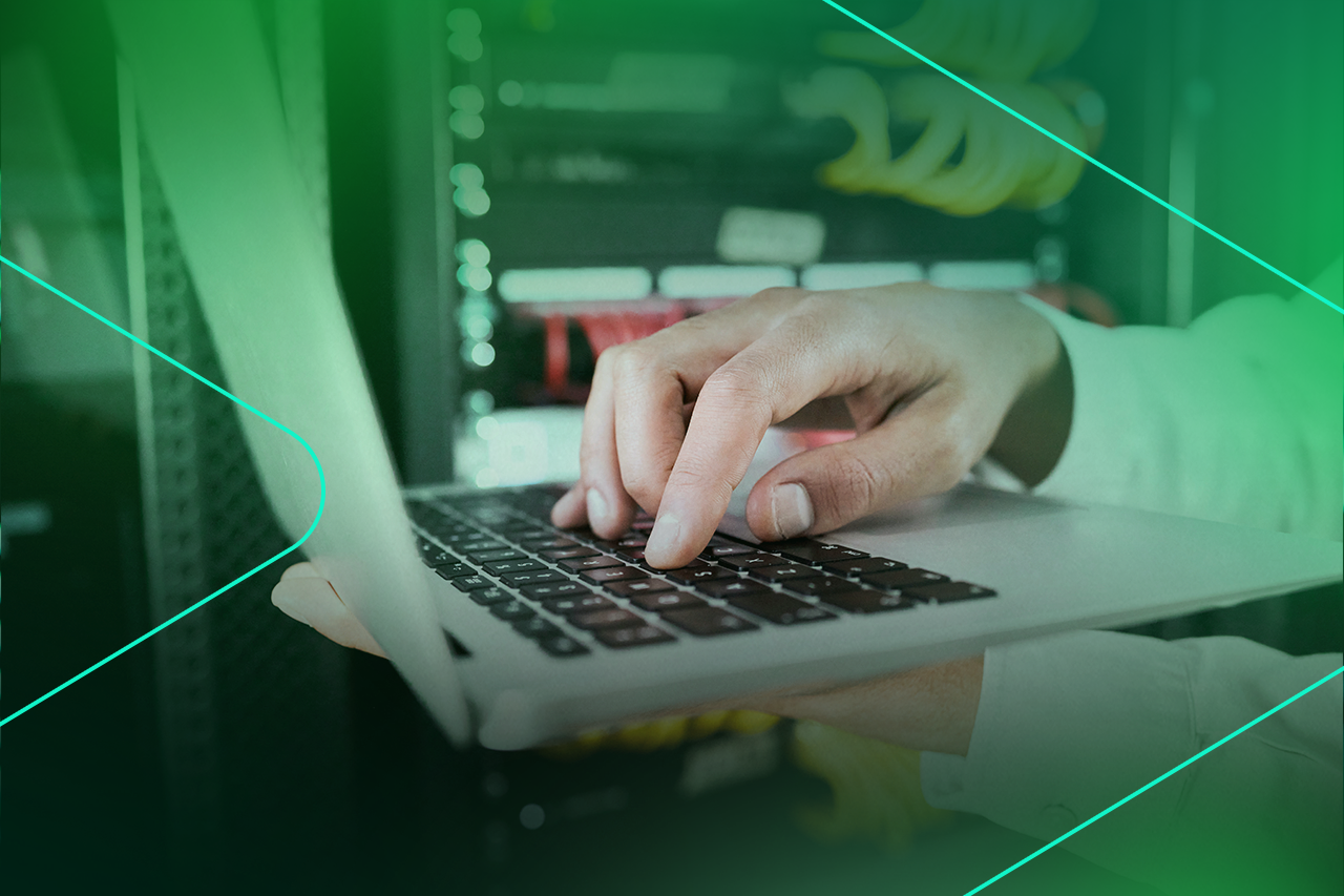 Mão digitando em um laptop com servidores ao fundo