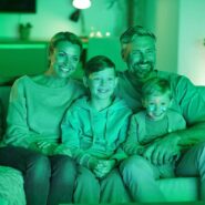 Família feliz assistindo TV em ambiente iluminado.