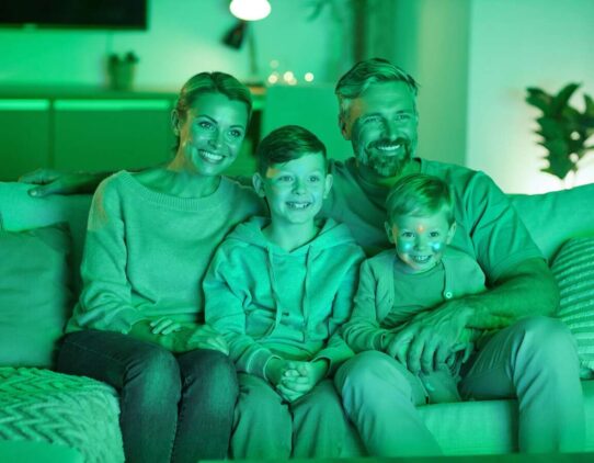 Família feliz assistindo TV em ambiente iluminado.