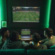 Grupo assistindo futebol em casa com laptop e TV.