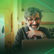 Homem com barba sorrindo enquanto usa laptop.