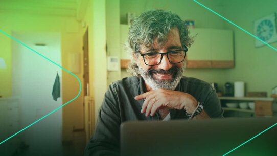 Homem com barba sorrindo enquanto usa laptop.