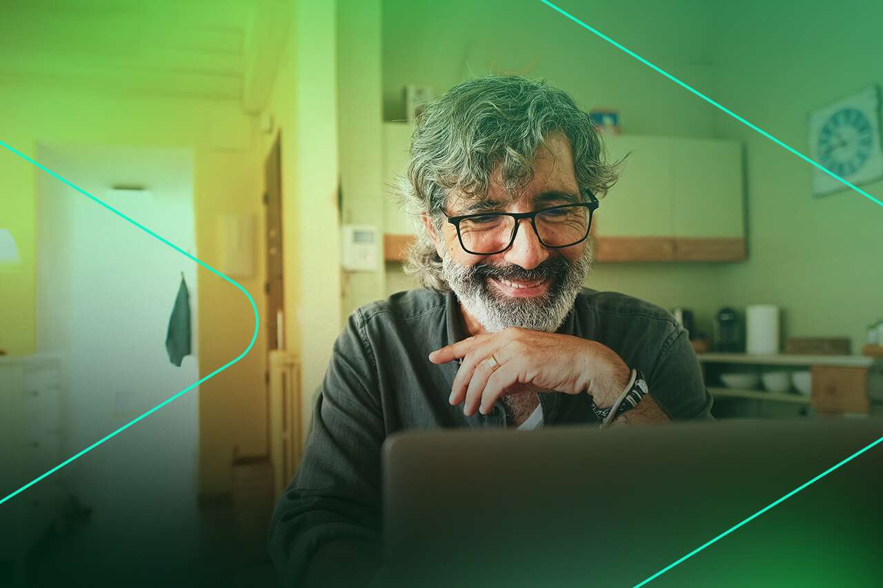 Homem com barba sorrindo enquanto usa laptop.