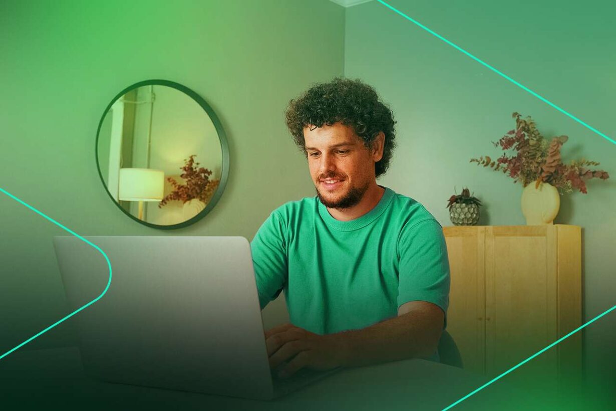 Homem sorrindo enquanto trabalha no laptop em casa.