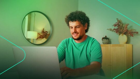 Homem sorrindo enquanto trabalha no laptop em casa.